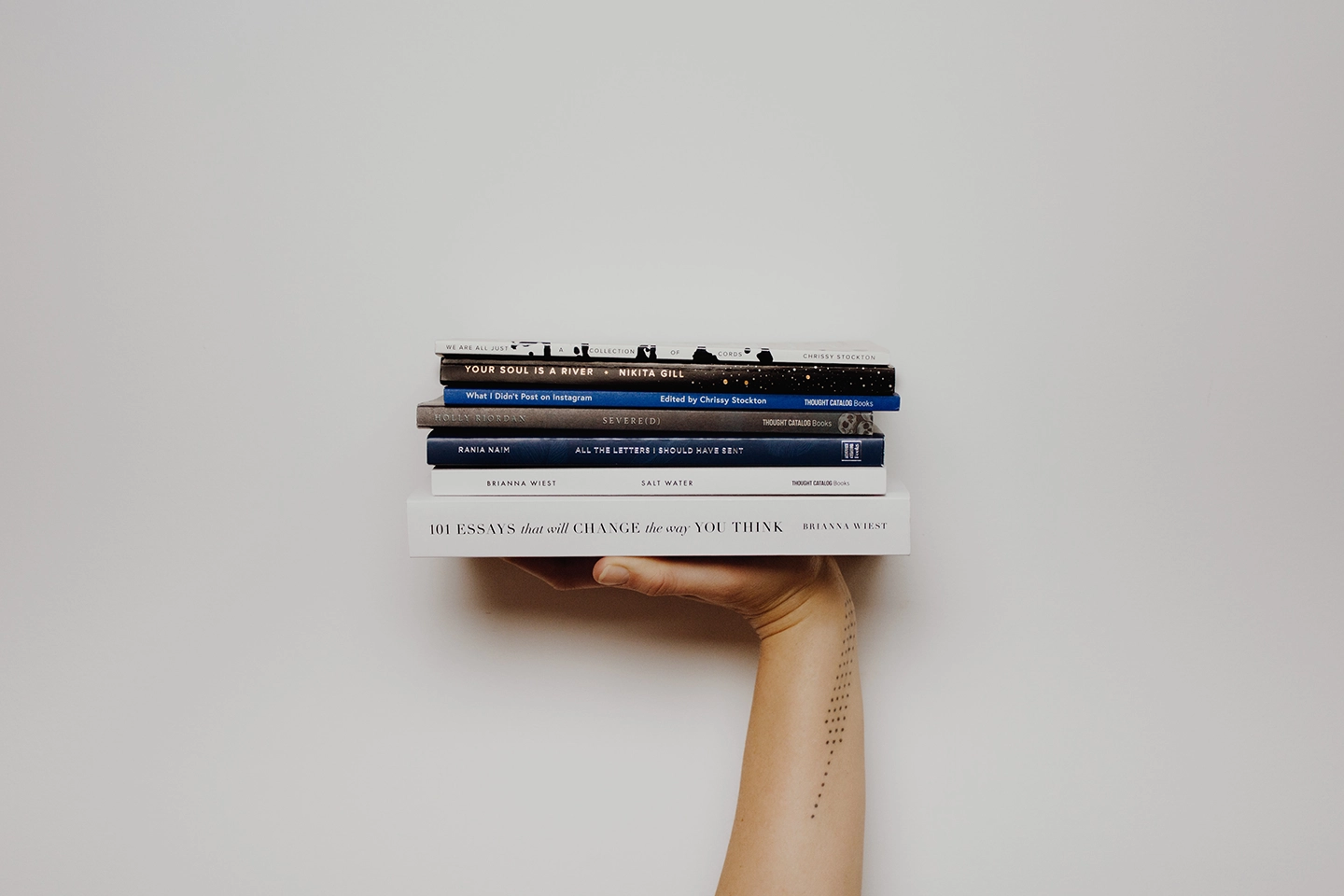 Eine Hand hält einen Stapel von fünf Büchern gegen einen hellen Hintergrund.