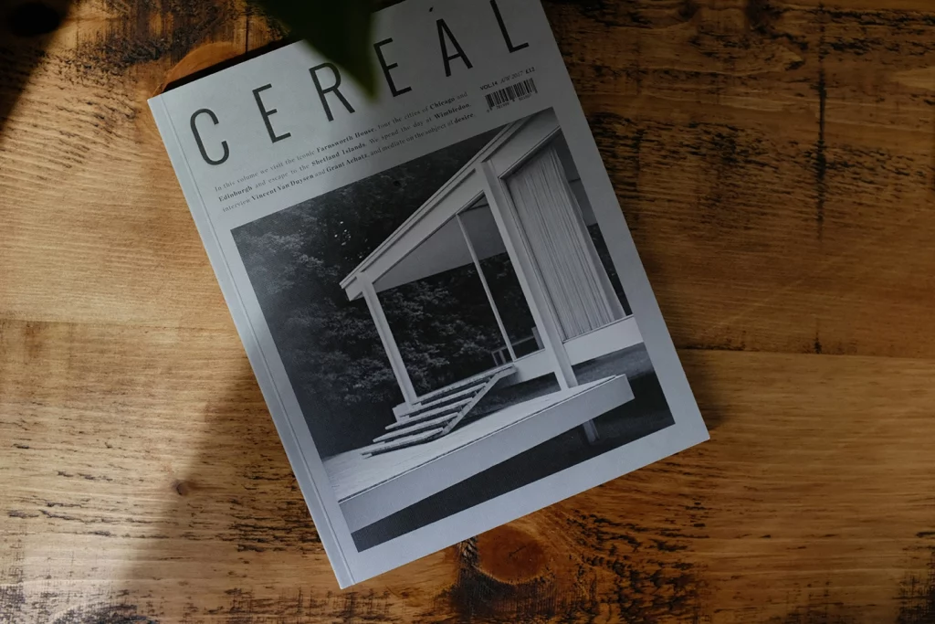 Auf einem rustikalen Holztisch liegt eine Zeitschrift mit dem Titel "CEREAL", das Cover zeigt ein monochromes Bild einer Veranda. Es steht für minimalistische, stilvolle Gestaltung.
