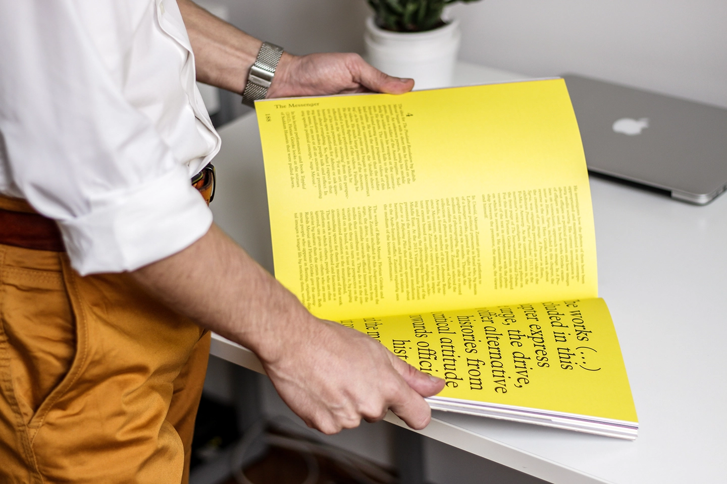 Person hält ein geöffnetes Magazin mit gelben Seiten und Text.
