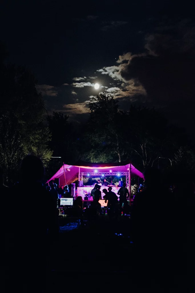 Feiernde Menschen vor einer beleuchteten Musikbühne bei Nacht mit Vollmond am Himmel beim Festungssommer Festival