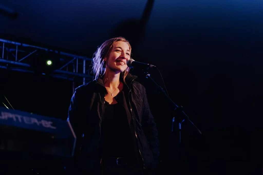 Lächelnde Sängerin im Scheinwerferlicht auf der Bühne bei einem nächtlichen Konzert beim Festungssommer Festival