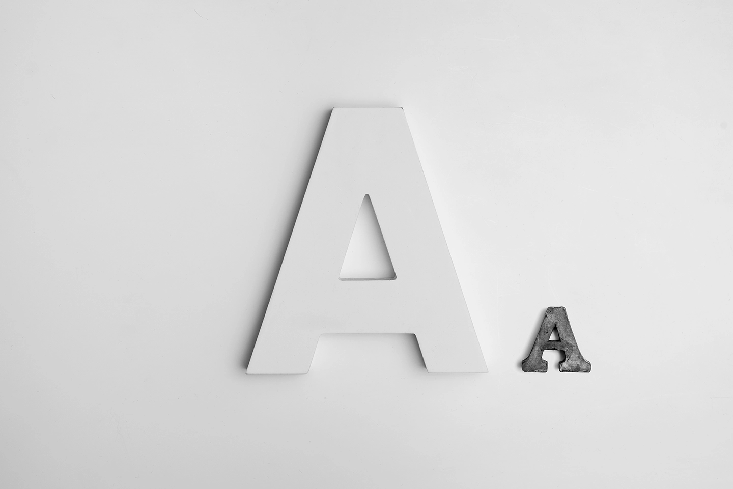 Buchstabe „A“ in Versalien einmal in weiß und groß, daneben in dunkelgrau und kleiner.